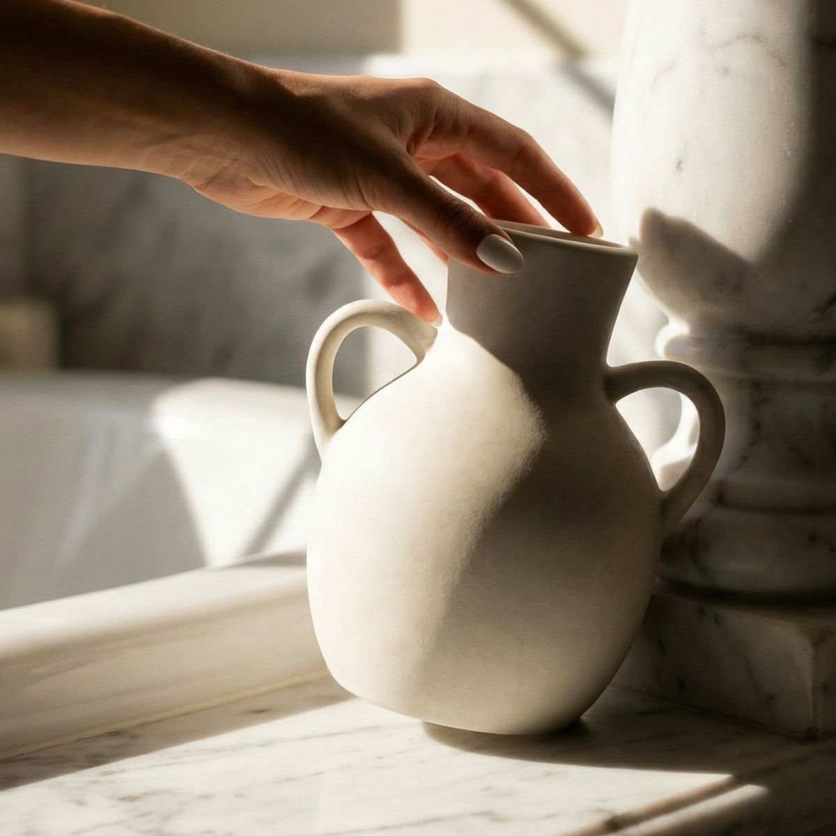 Person holding a white ceramic vase on a marble surface with soft lighting