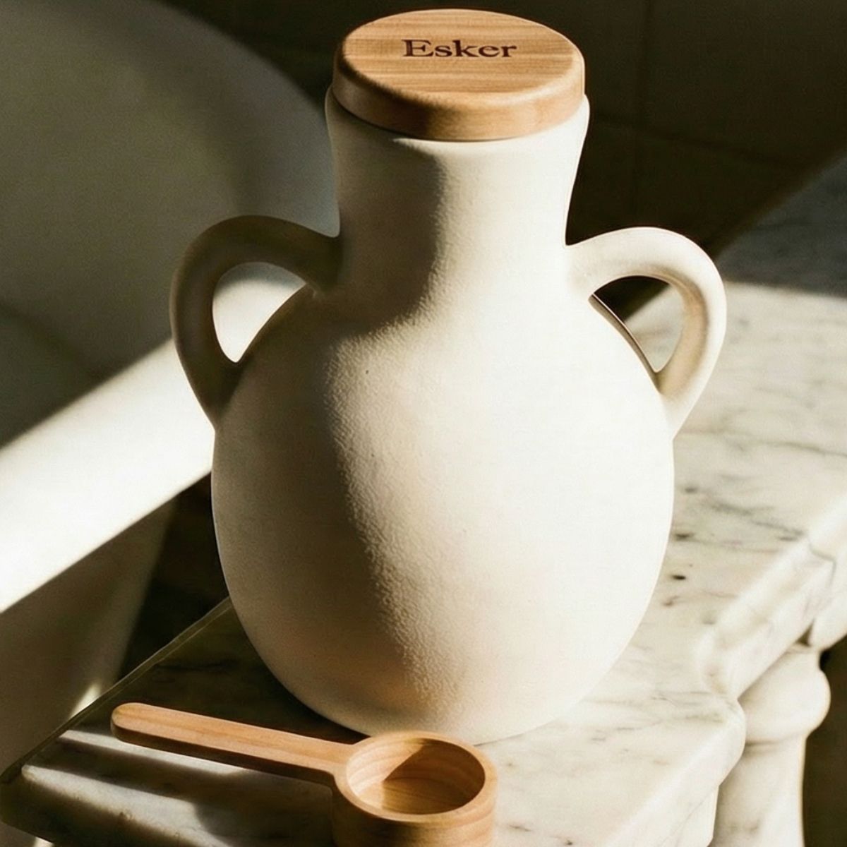 White ceramic jar with wooden lid and spoon on a marble surface