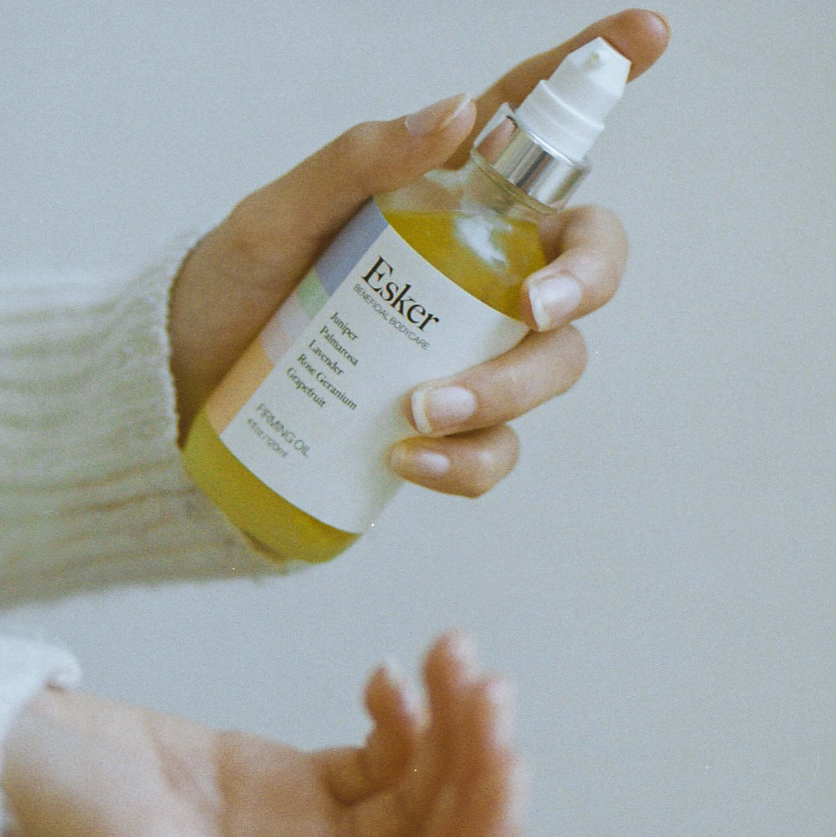 Spraying Esker Firming Oil Deluxe Mini into cupped hands