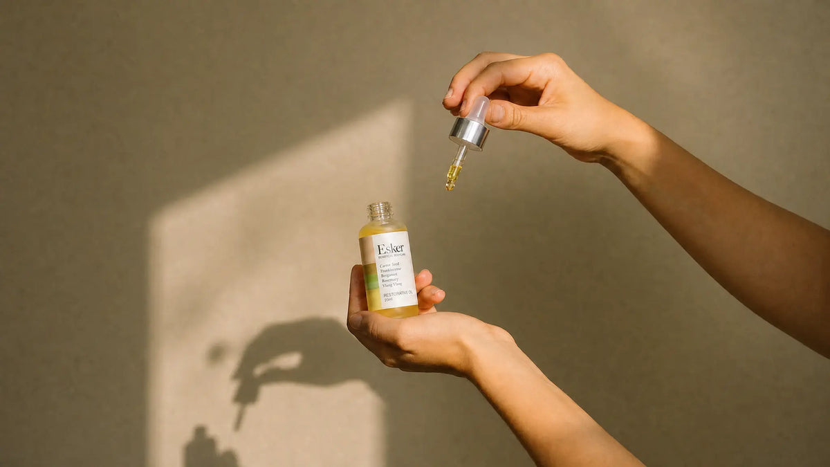 Dispensing Esker Restorative Oil Deluxe Mini from the dropper into an open hand