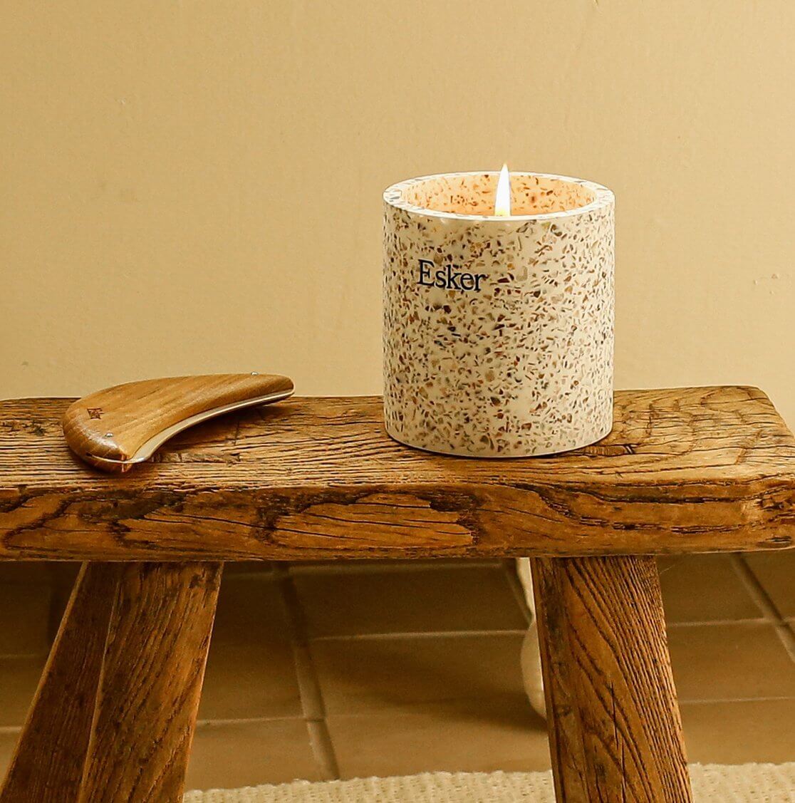 Esker Terrazzo Plantable Candle glowing on a rustic wooden stool