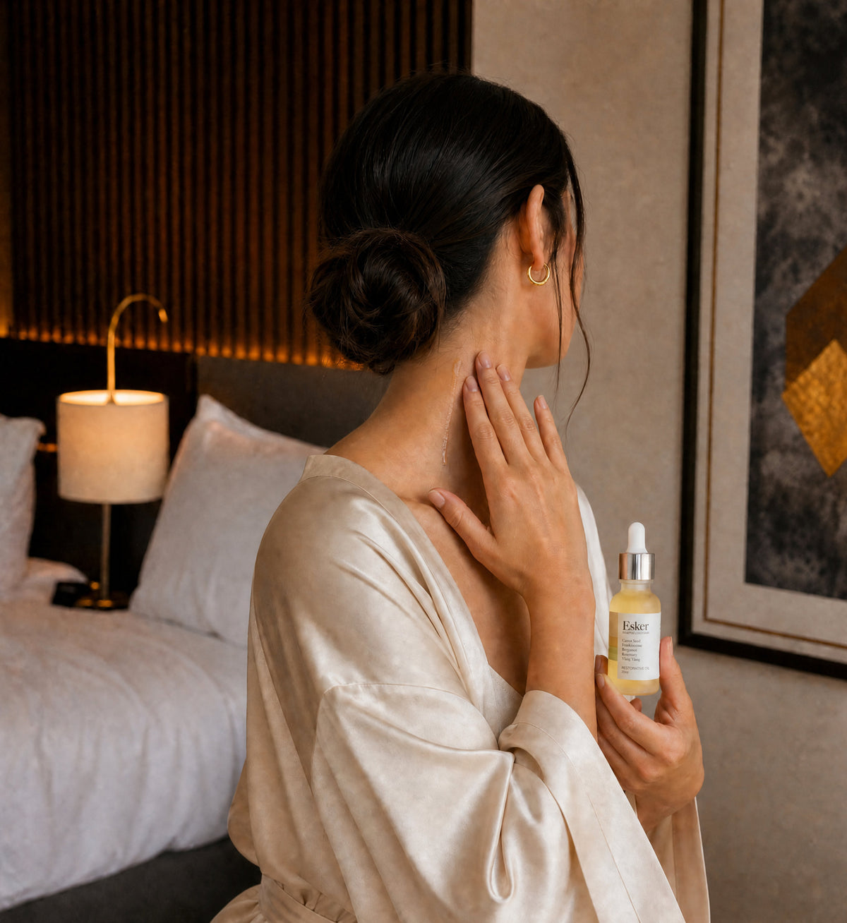 Woman in a robe applying Esker Restorative Oil Deluxe Mini to her neck